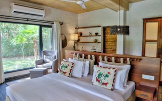 Habitación de hotel con una cama grande, una silla, una mesita de noche, una lámpara, una estantería con adornos y vistas al exterior.
