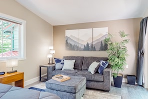 A modern living room with a grey sofa, a wooden side table, a coffee table, and a large potted plant. - Rare, dog-friendly riverfront retreat with hot tub access plus kayaks & AC (Tahuya)