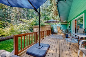 A wooden deck with outdoor furniture, including a table and chairs, and umbrellas providing shade. - Rare, dog-friendly riverfront retreat with hot tub access plus kayaks & AC (Tahuya)