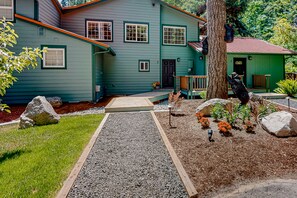 A two-story house with a green exterior, a wooden deck, and a gravel pathway leading to the front door. - Rare, dog-friendly riverfront retreat with hot tub access plus kayaks & AC (Tahuya)
