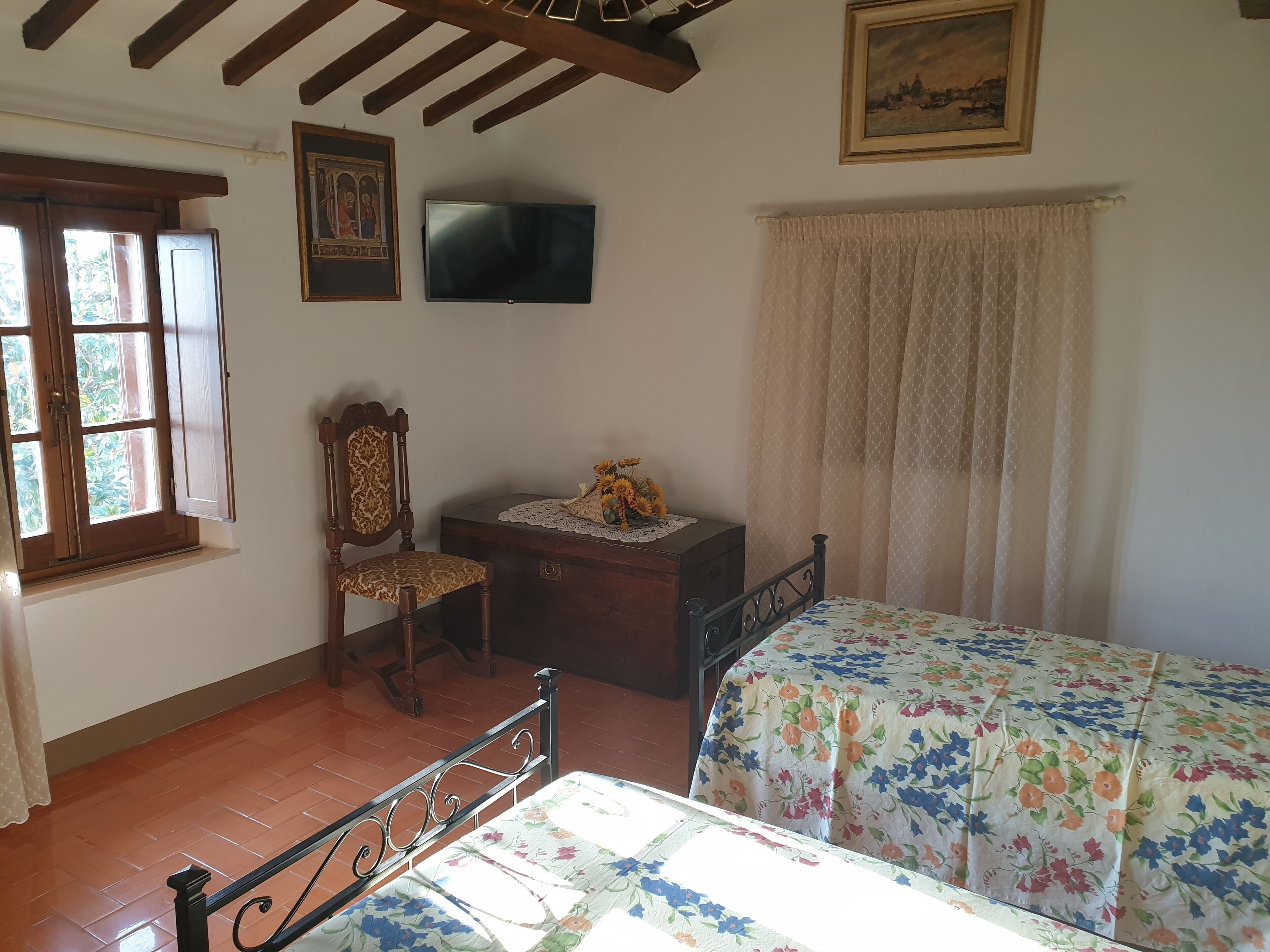 A bedroom with a bed, a chair, a dresser, a television, and a window with curtains.