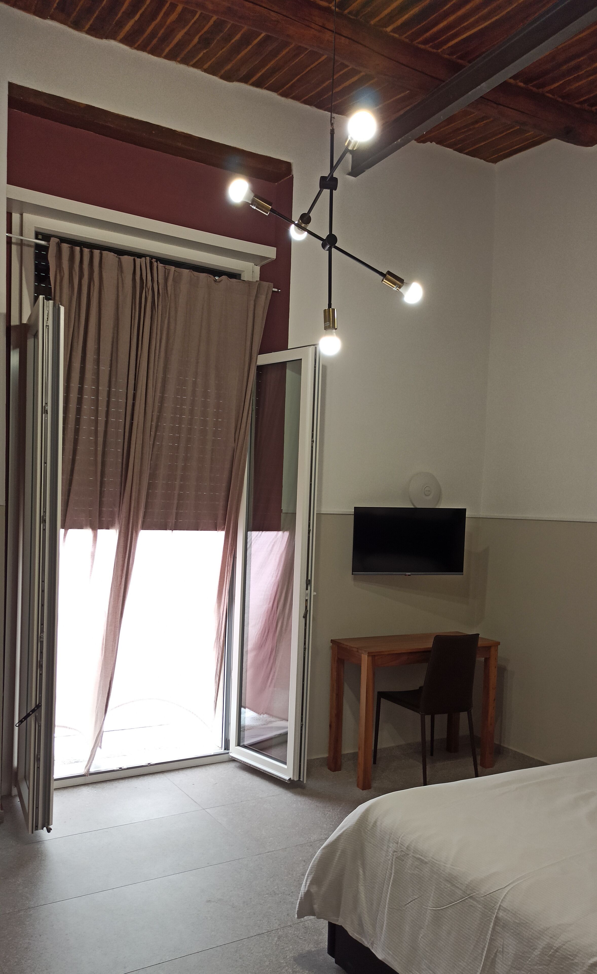 A bedroom with a bed, a desk, a chair, a TV, and a ceiling light fixture.