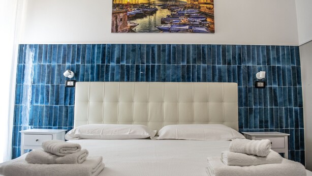 A hotel room with a large bed, two nightstands, and a wall-mounted painting of a harbor scene. - La Suite del Centro Storico (Naples)