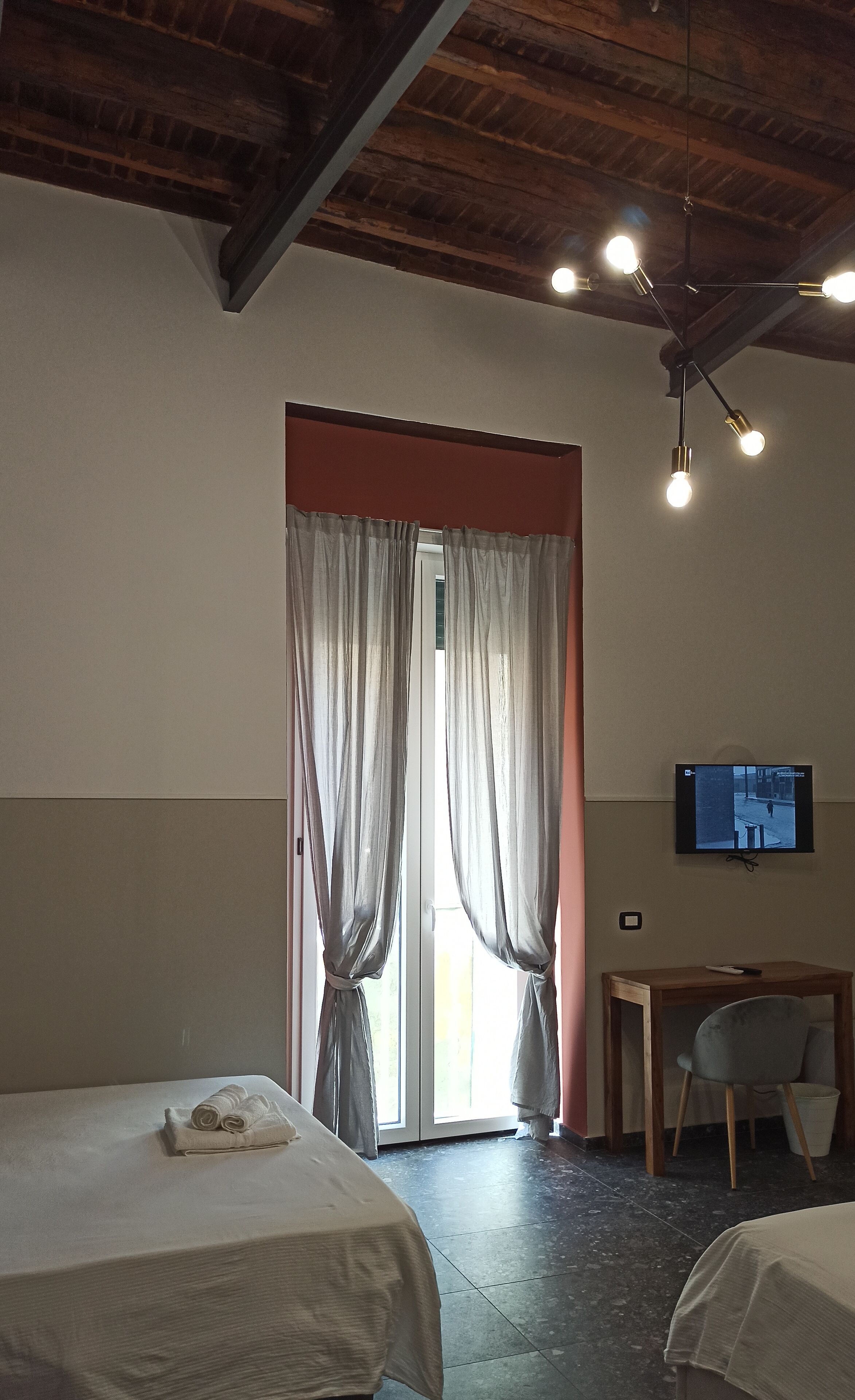 A hotel room with two beds, a desk with a chair, a television on the wall, and a window with curtains.