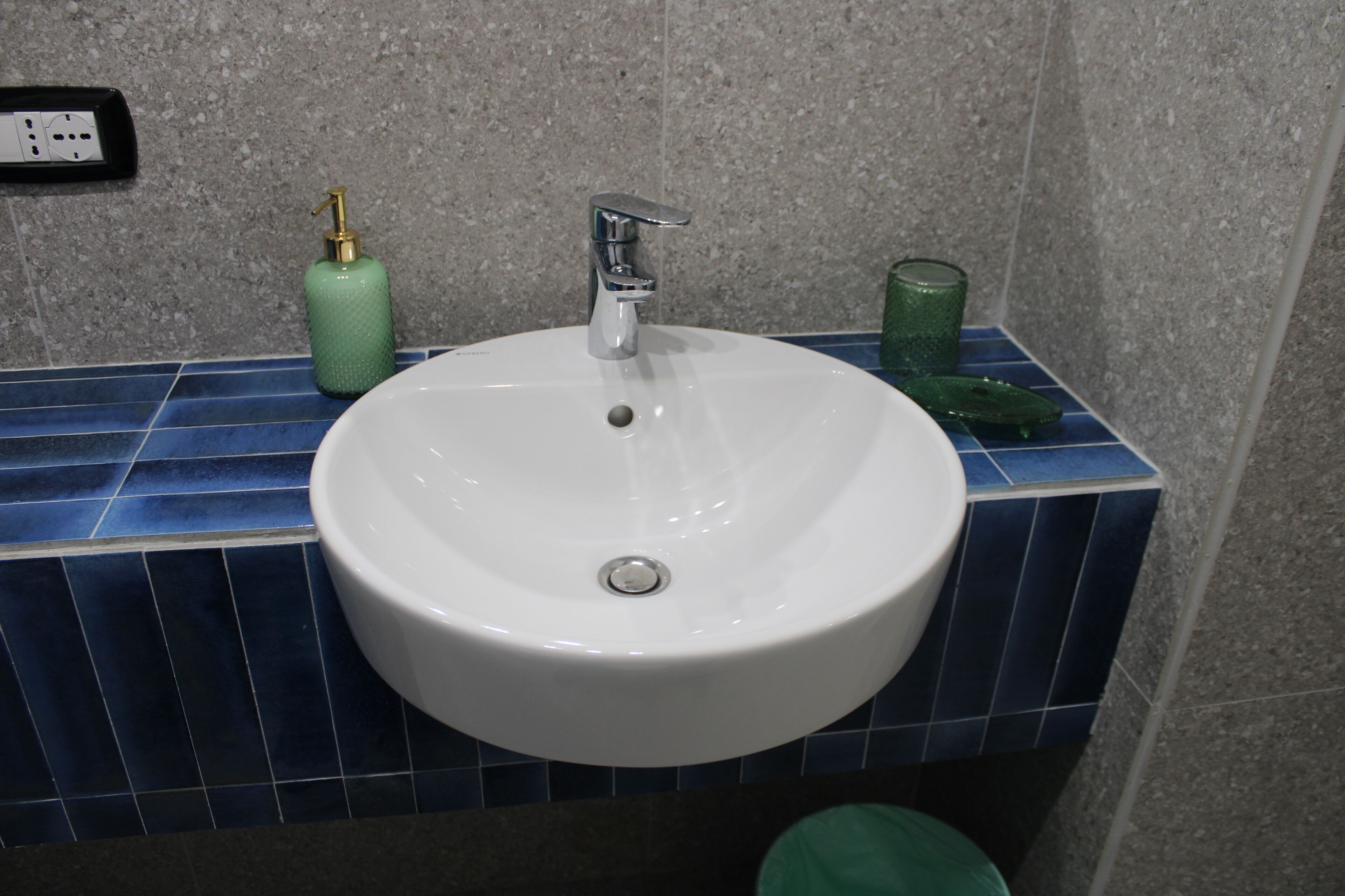 Un lavamanos con grifo cromado, un dispensador de jabón verde y un vaso de vidrio verde.