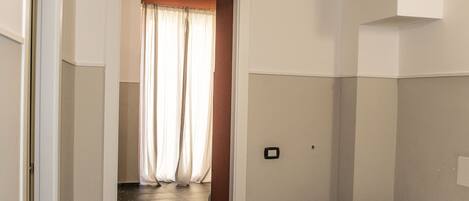 A narrow hallway leading to a bedroom with a bed and a window with curtains.
