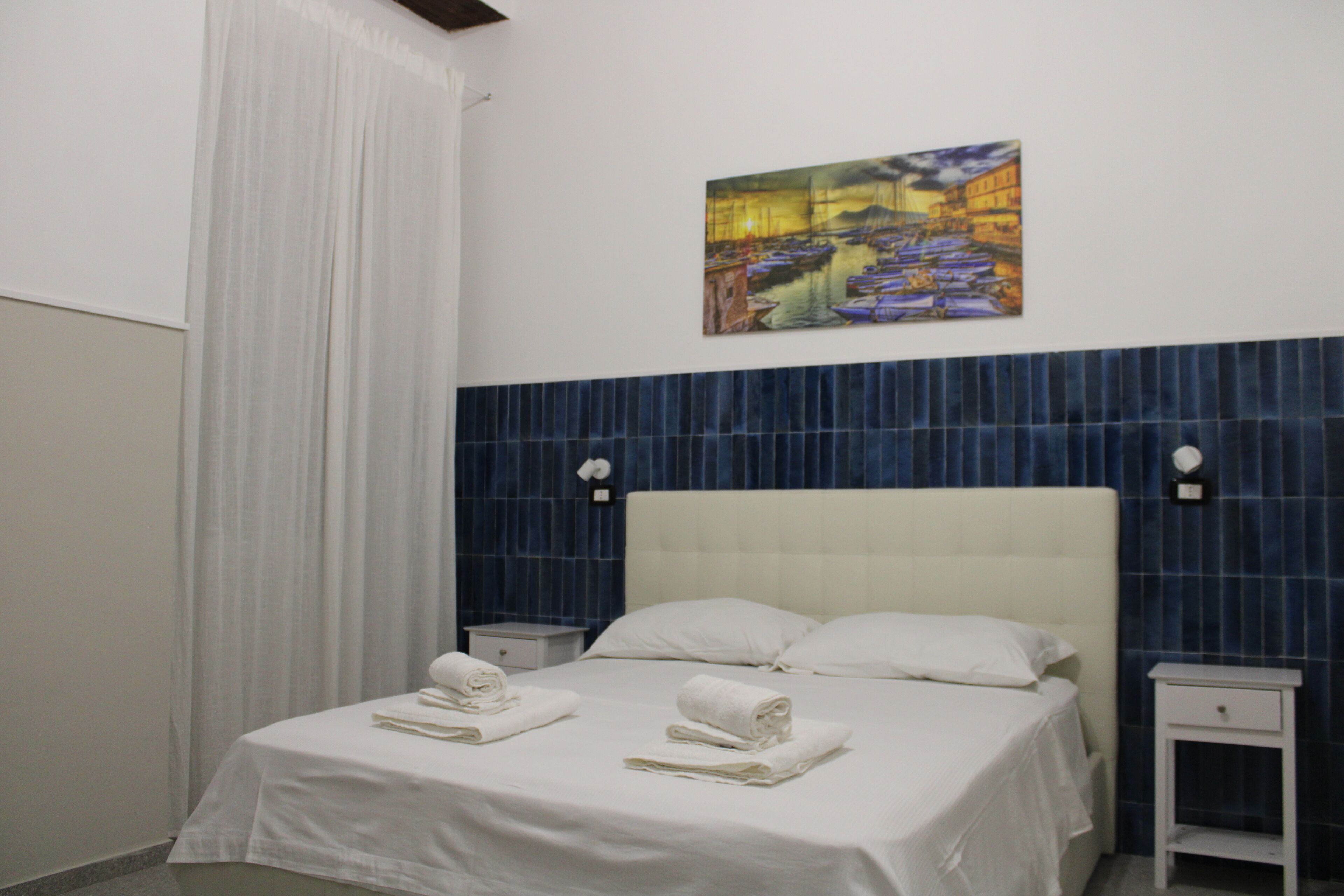 Une chambre d’hôtel avec un lit, des rideaux blancs, un tableau au mur et un mur d’accent recouvert de carreaux bleus.