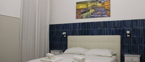 Une chambre d’hôtel avec un lit, des rideaux blancs, un tableau au mur et un mur d’accent recouvert de carreaux bleus.