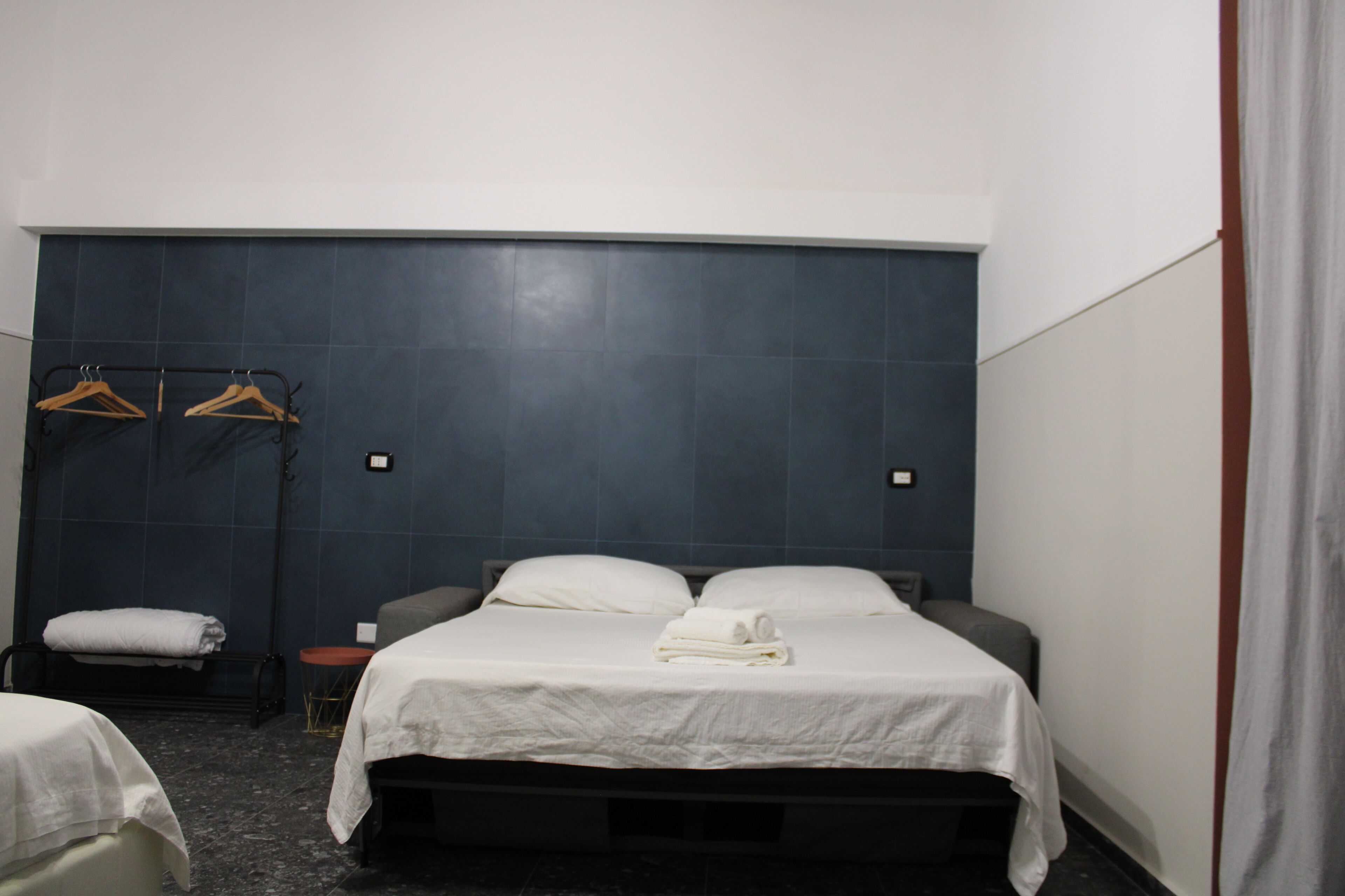 Quarto de hotel com uma cama grande, duas mesas de cabeceira, uma mesinha redonda e um porta-toalhas fixado na parede.