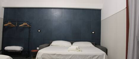 Quarto de hotel com uma cama grande, duas mesas de cabeceira, uma mesinha redonda e um porta-toalhas fixado na parede.