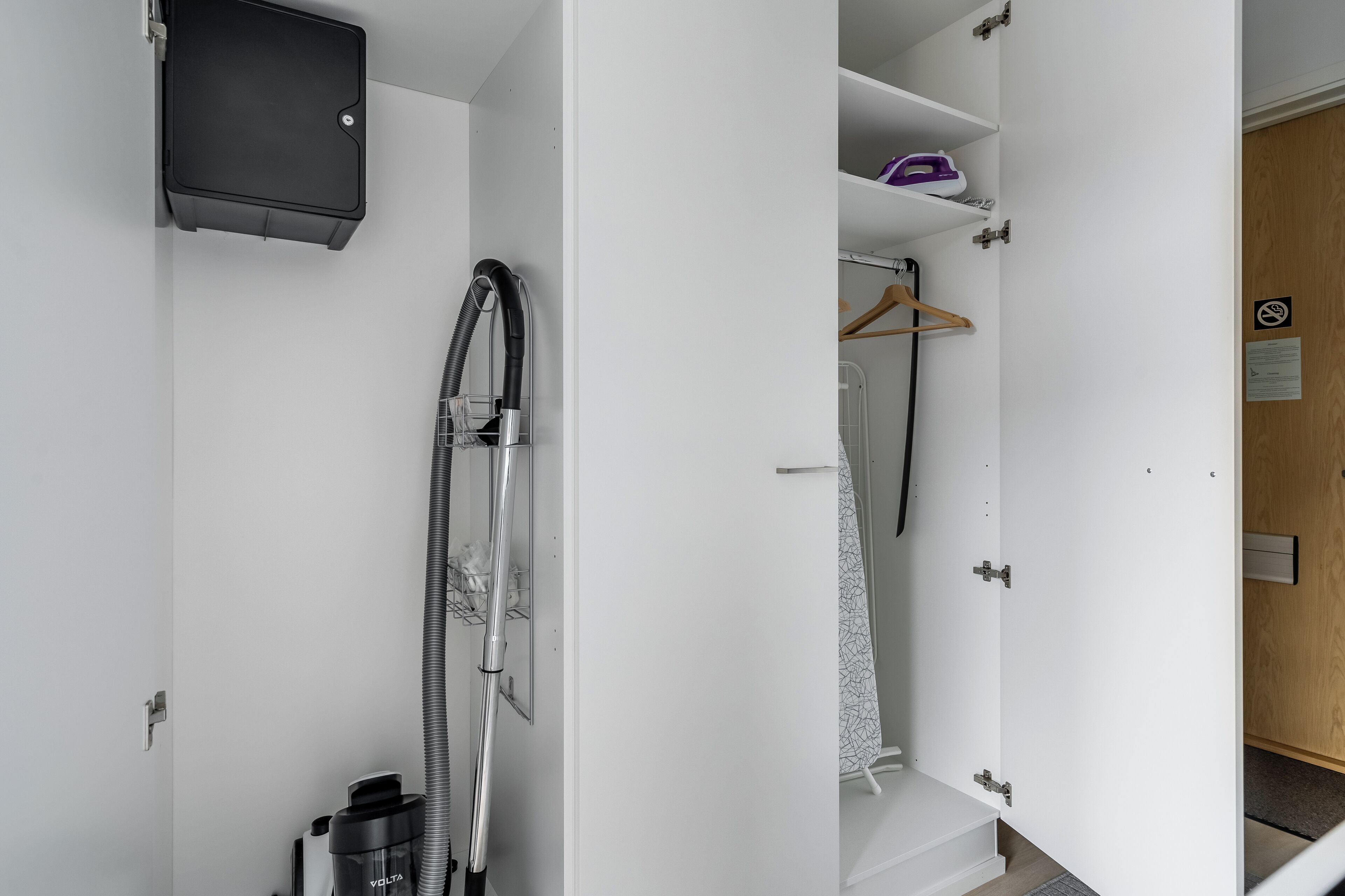 A compact, modern bathroom with a built-in shower, a vacuum cleaner, and a small storage cabinet.