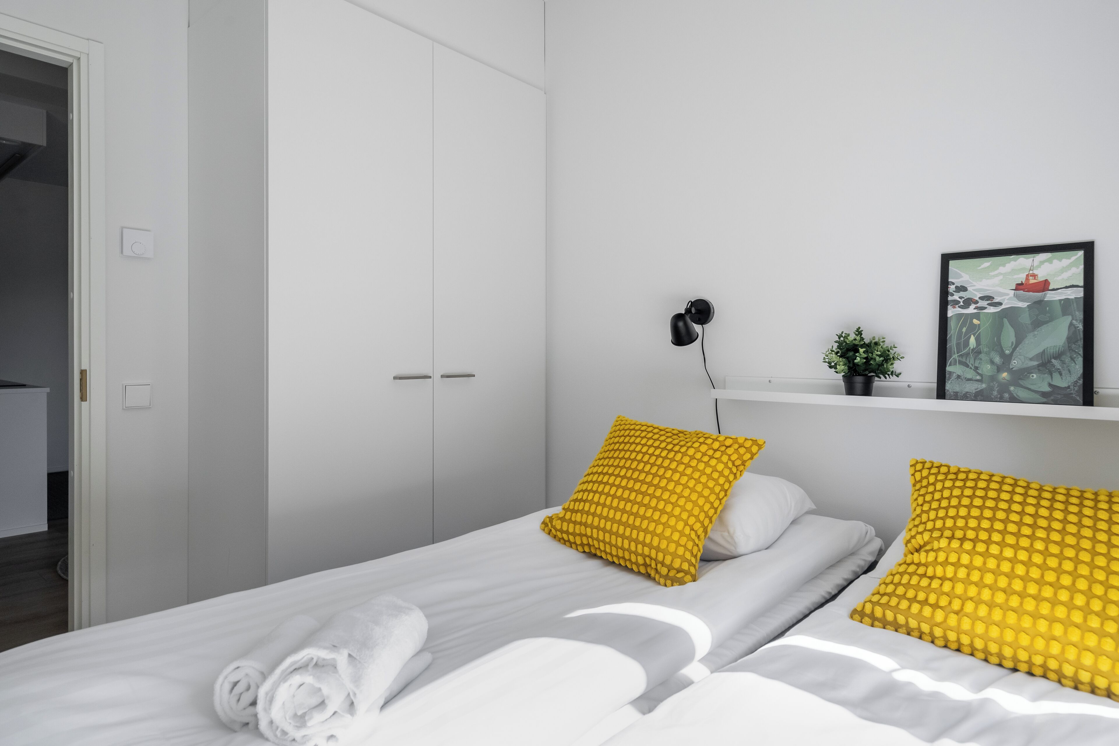 Un dormitorio moderno con una cama, dos almohadas, una mesita de noche, una lámpara de pared y un cuadro enmarcado.
