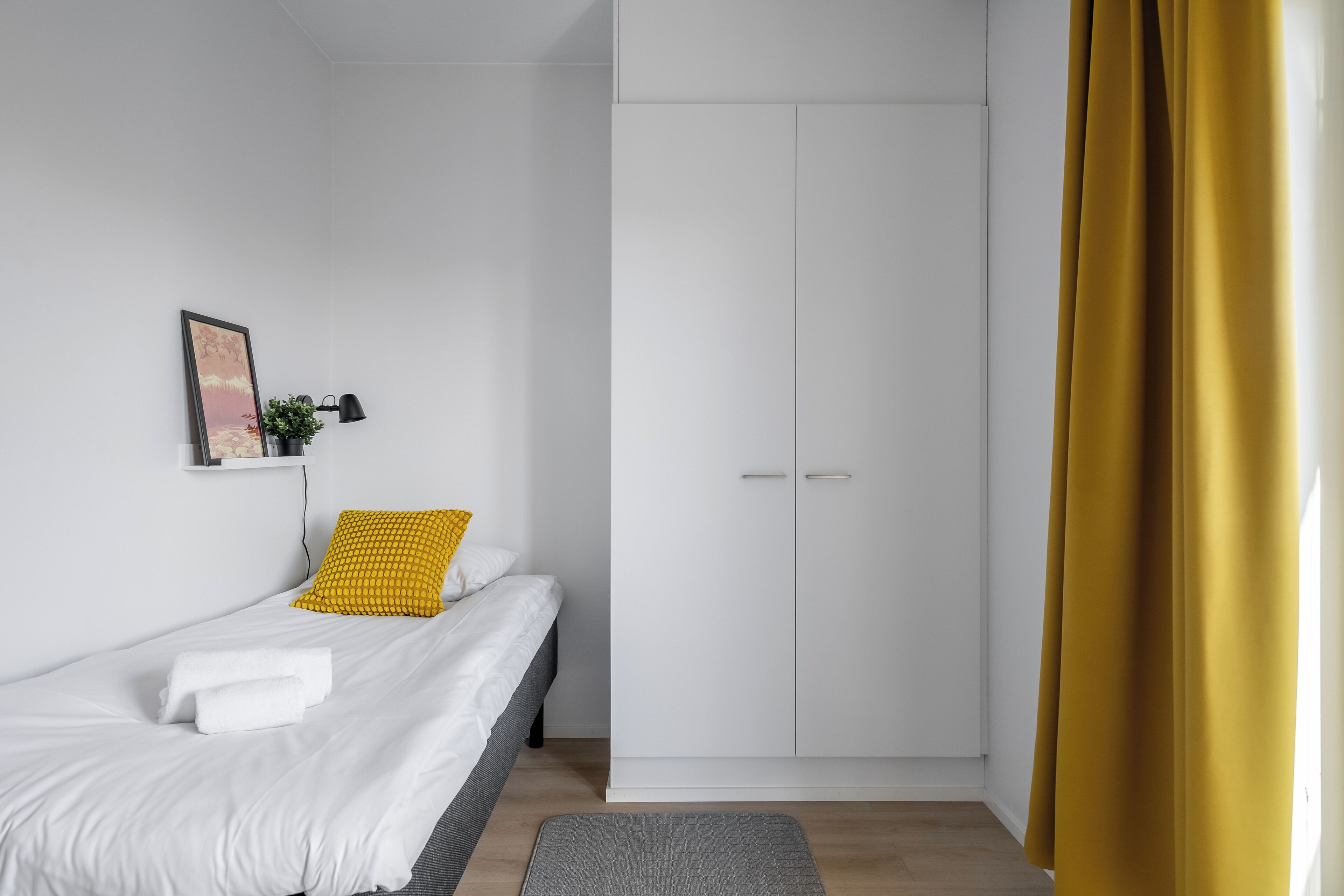 A bedroom with a bed, a wardrobe, a bedside table with a lamp, and a window with curtains.