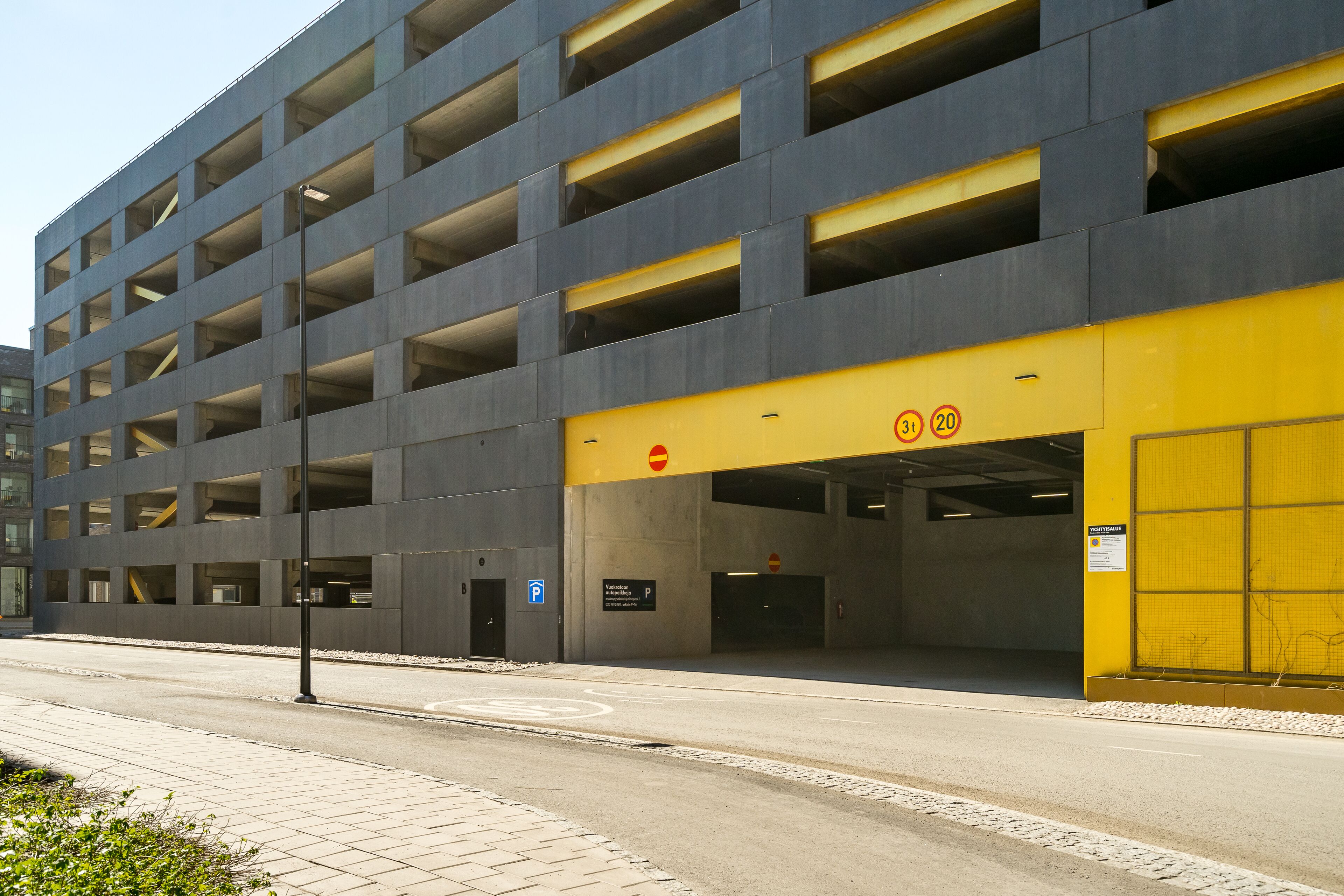 Un parking à étages doté d’une façade jaune et grise, de nombreuses places de stationnement et d’un chemin piétonnier bien défini.