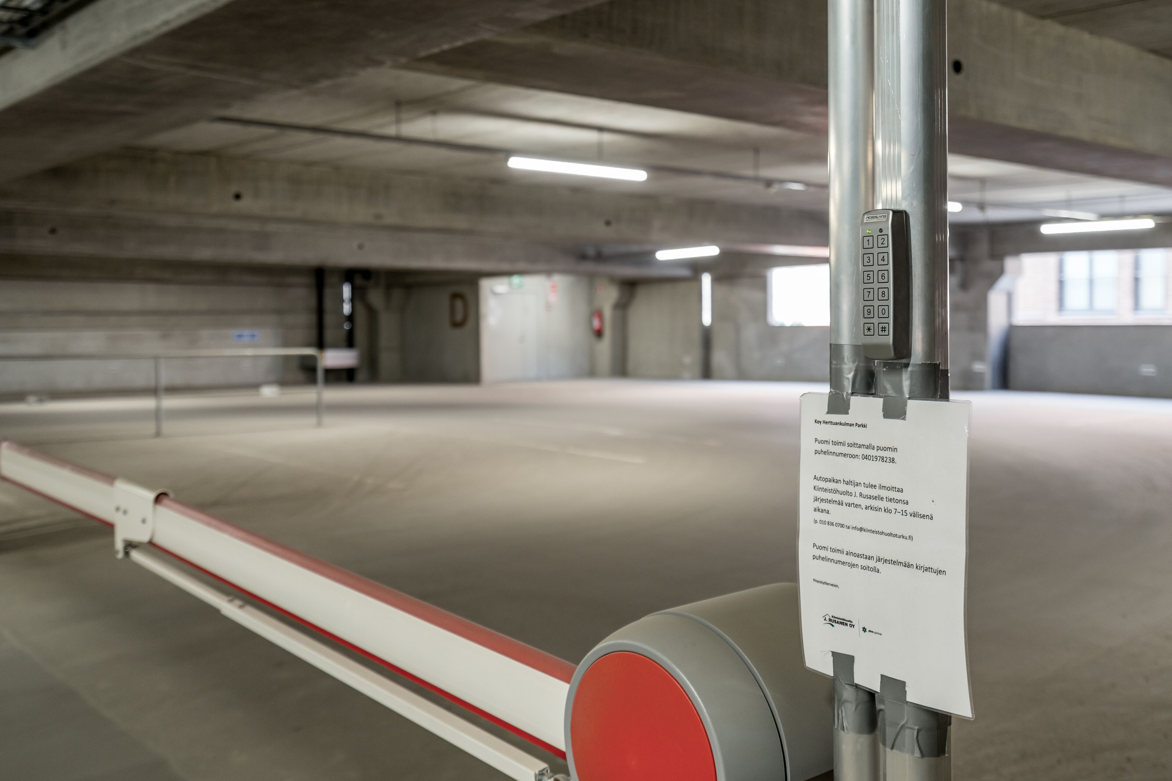 Un parking couvert doté d’une barrière d’accès rouge et blanche et d’un panneau avec du texte.
