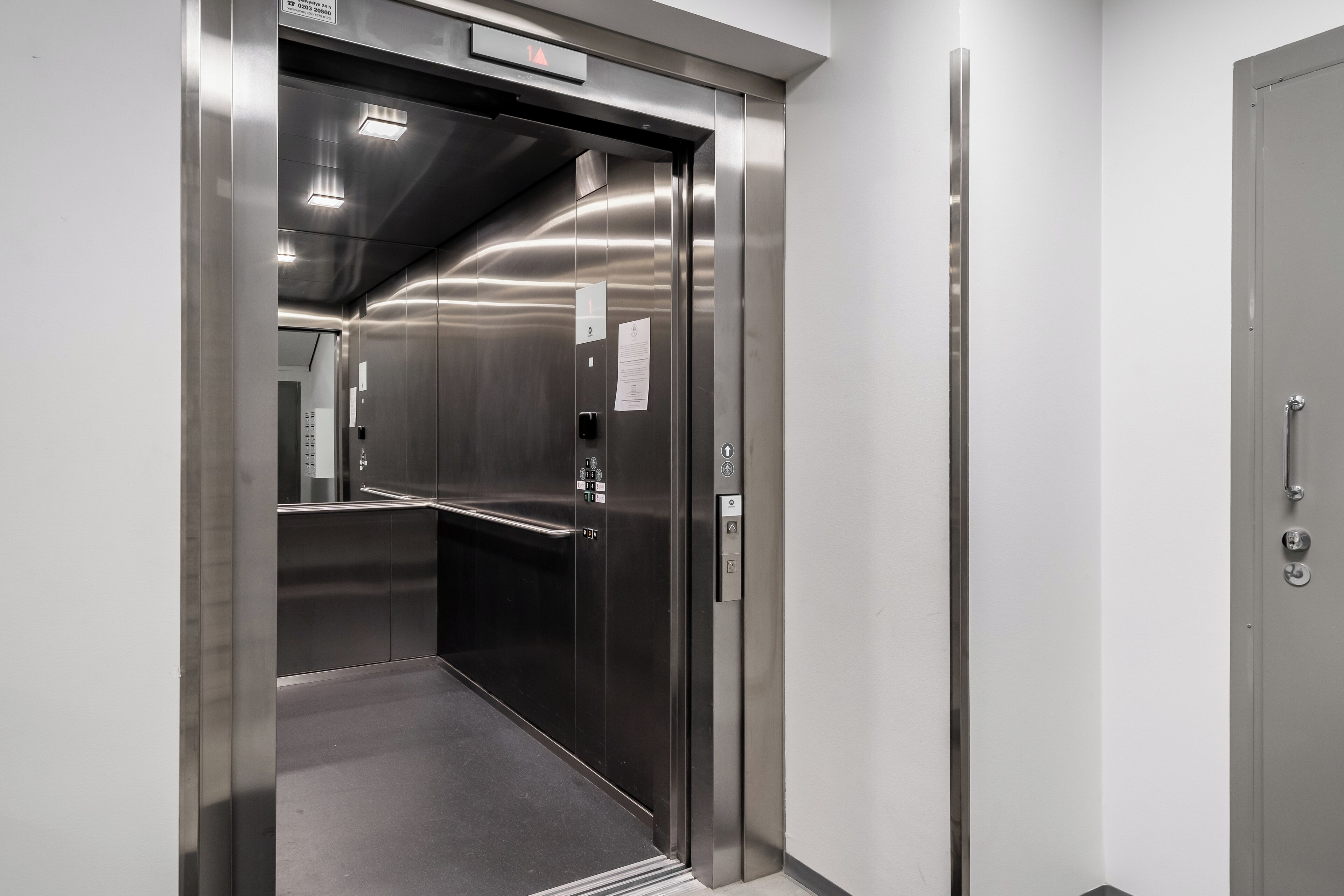 Un ascenseur moderne avec une finition métallique, un panneau de commande et un panneau indiquant la sortie de secours.