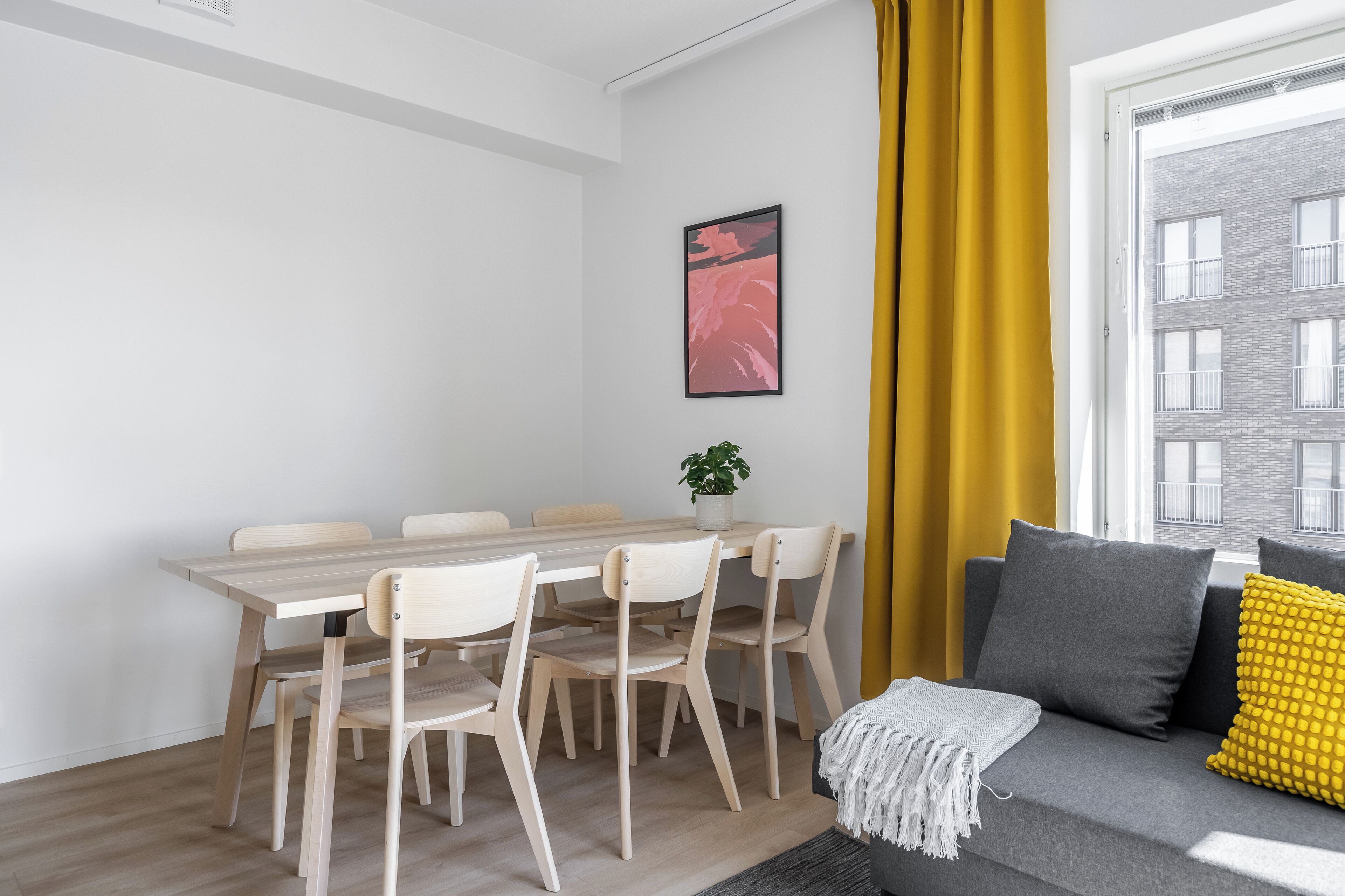 A modern living room with a grey sofa, yellow cushions, and a dining area with a wooden table and chairs.