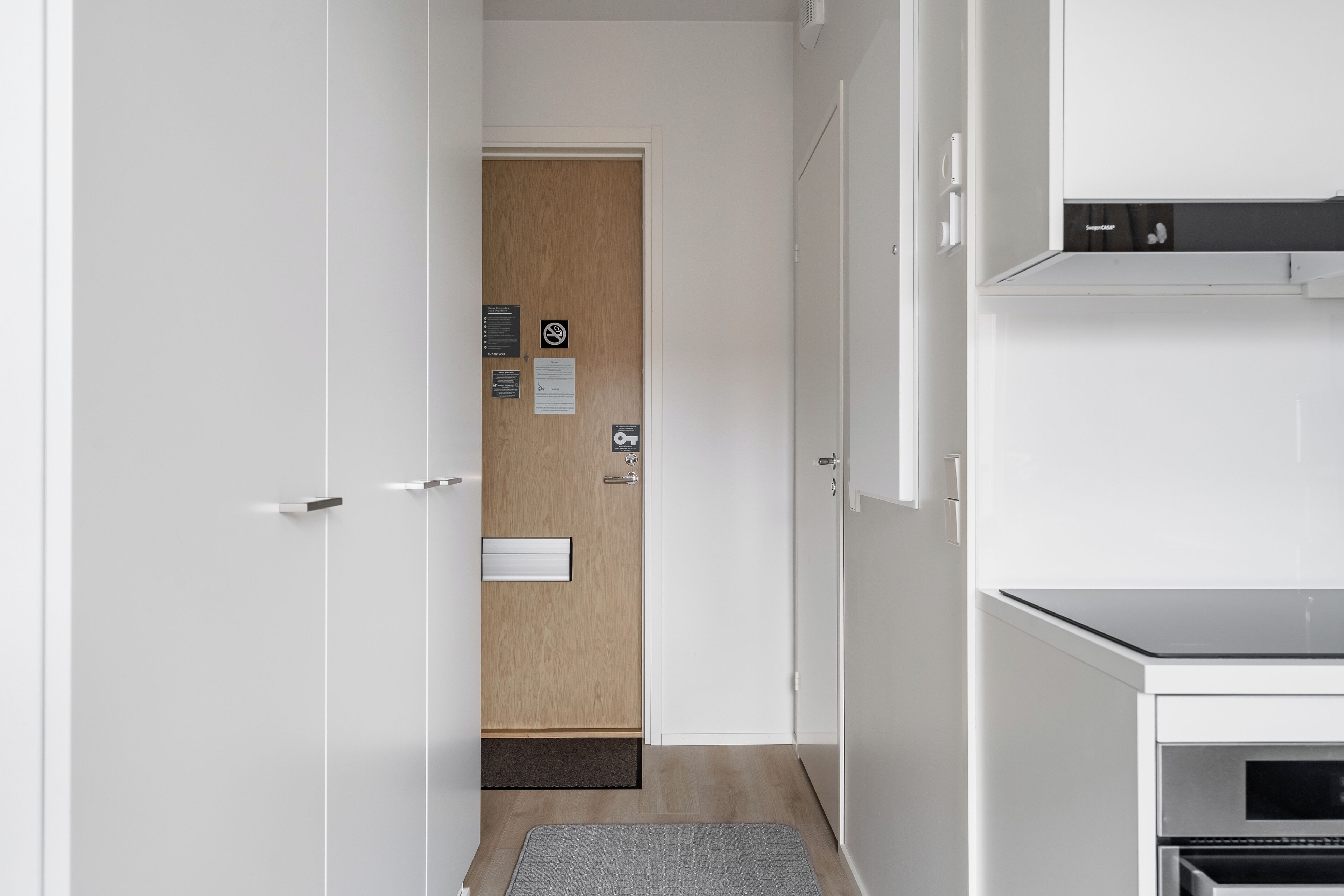 Una cocina moderna con armarios blancos, horno empotrado y una puerta de madera con felpudo.