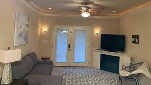 A living room with a sofa, a television, a fireplace, and a ceiling fan. - Lolly Gris-Gris (Hot Springs)