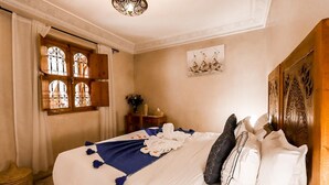 Una cama bien hecha con una manta azul y almohadas blancas, un cabecero de madera, un adorno en la pared y una ventana con cortina.