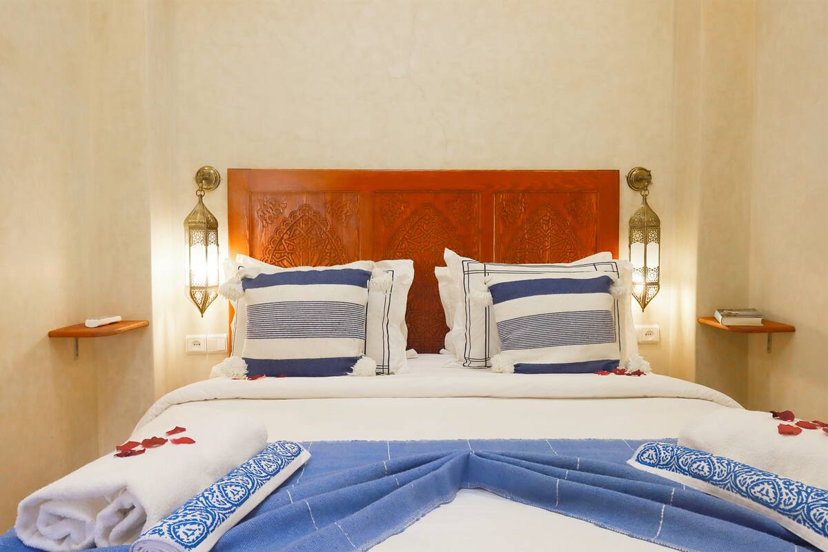 A neatly made bed with a wooden headboard, two wall-mounted lamps, and a small bedside table with a book.