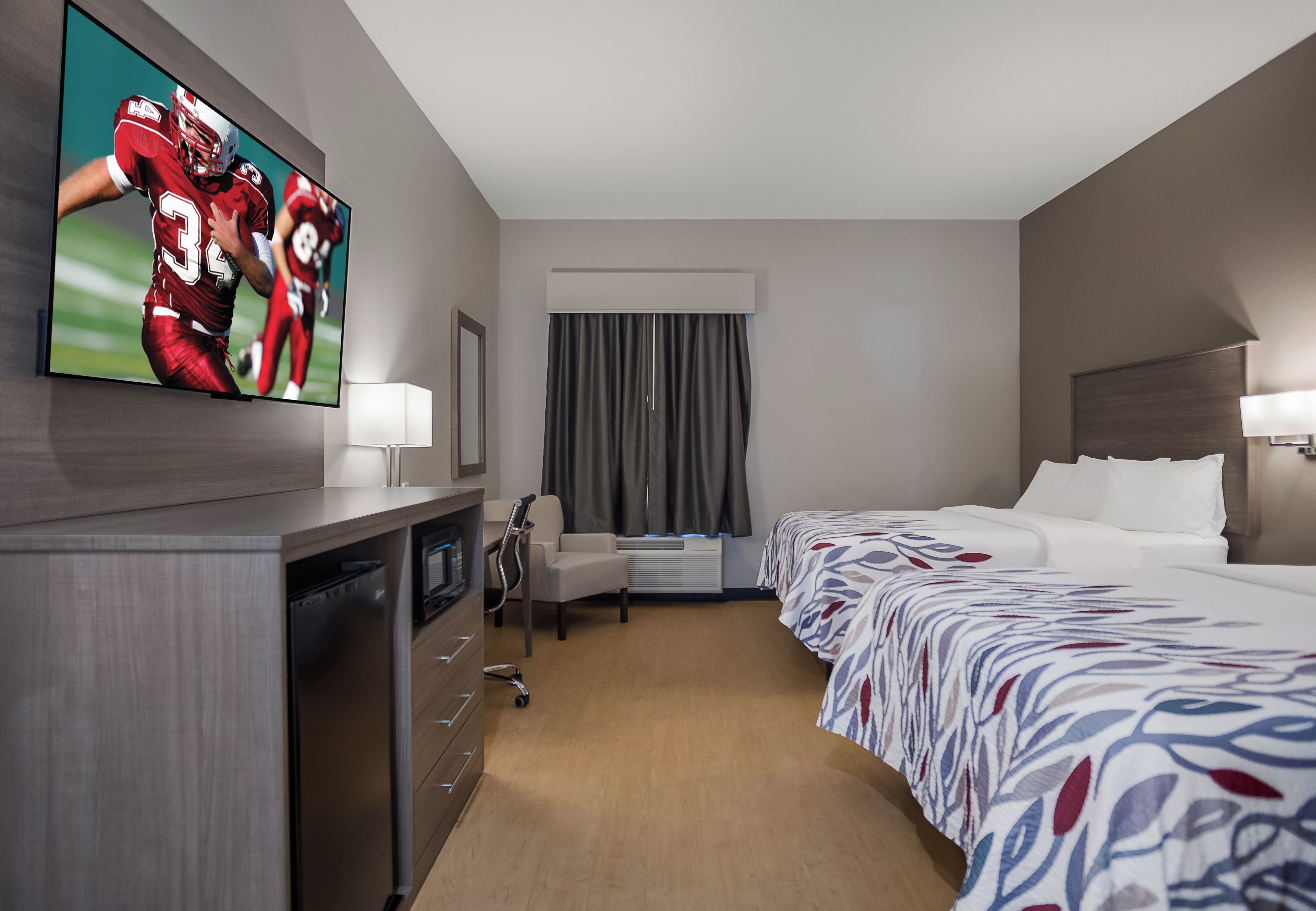 Ein Hotelzimmer mit Bett, Schreibtisch mit Computer, Wandfernseher und einem Fenster mit Vorhängen.