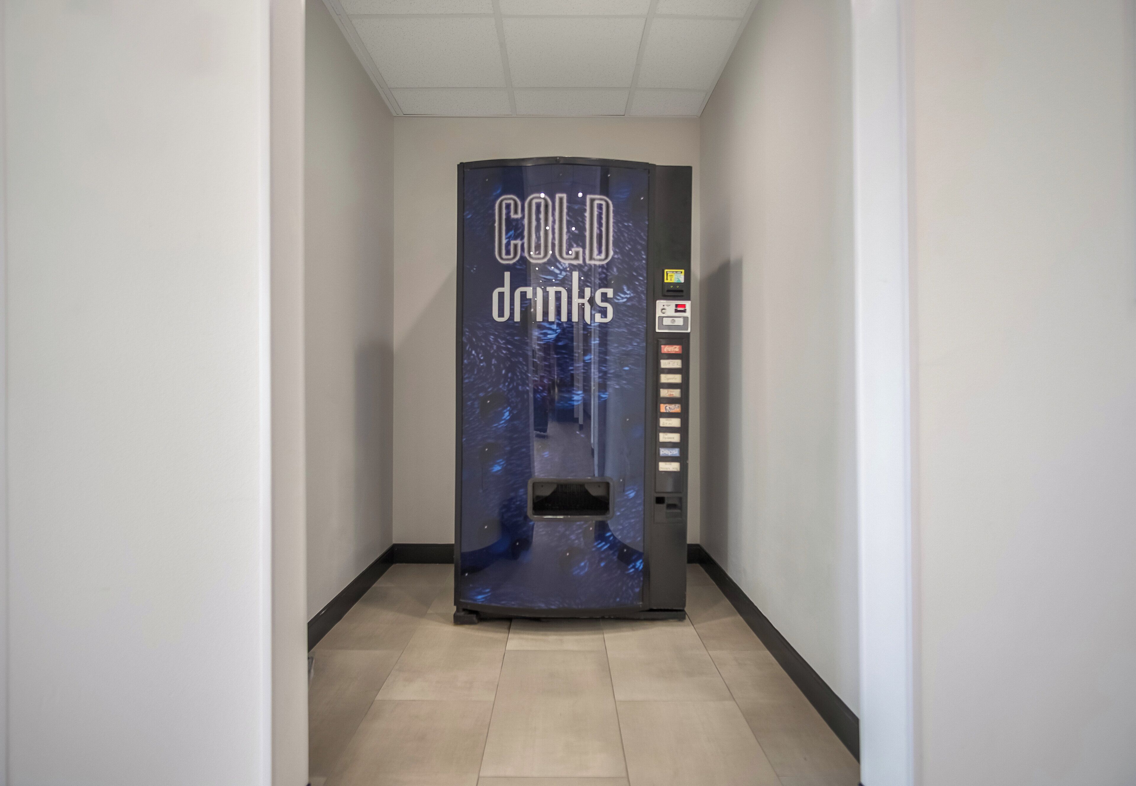 Ein Getränkeautomat mit der Aufschrift 'COLD drinks' in einem Korridor mit Fliesenboden.