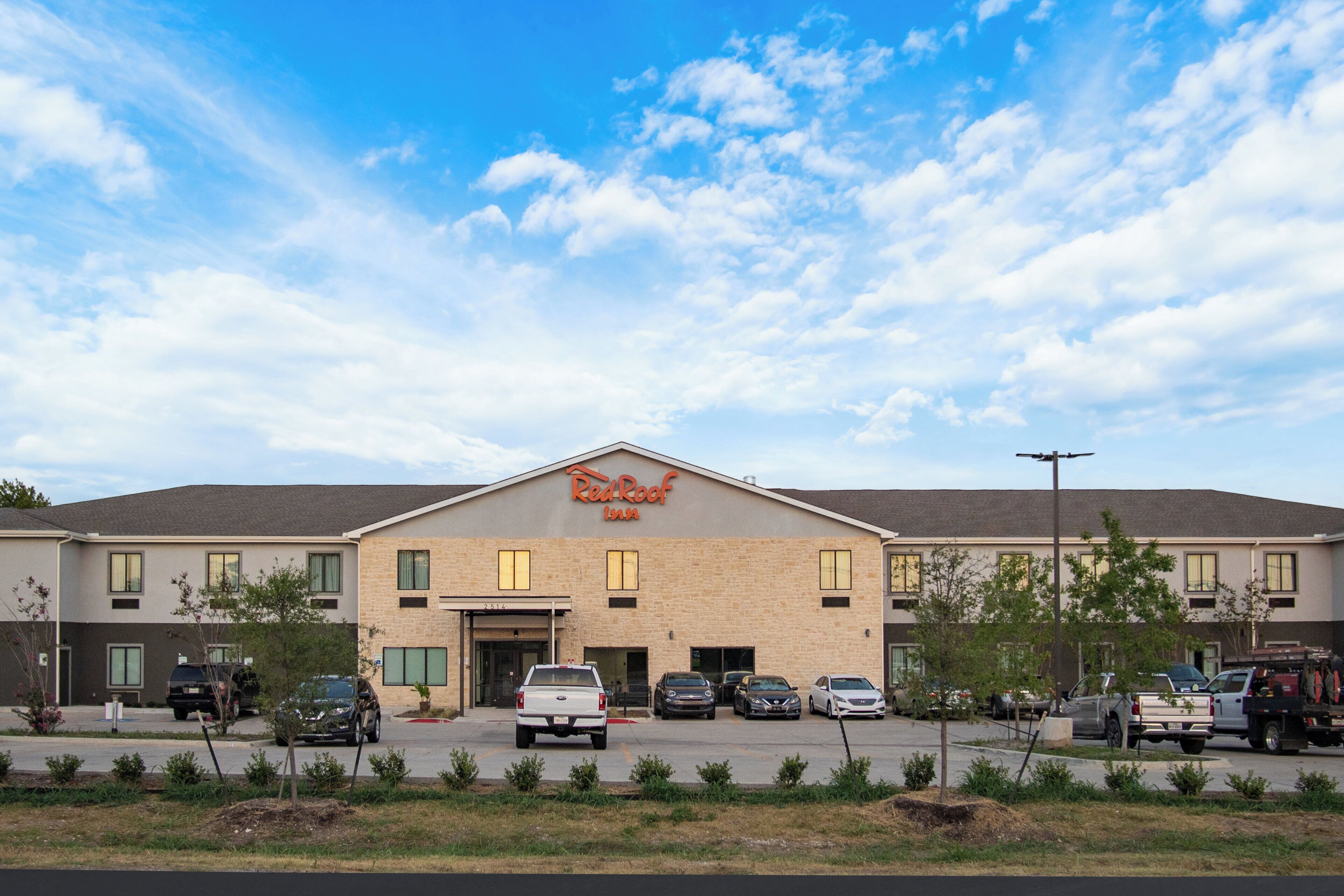 A Red Roof Inn with a parking lot in front, a clear sky, and a few cars parked.