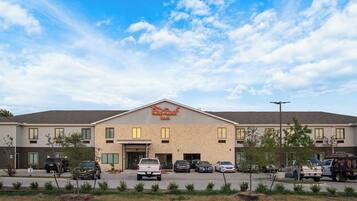 A Red Roof Inn with a parking lot in front, a clear sky, and a few cars parked.