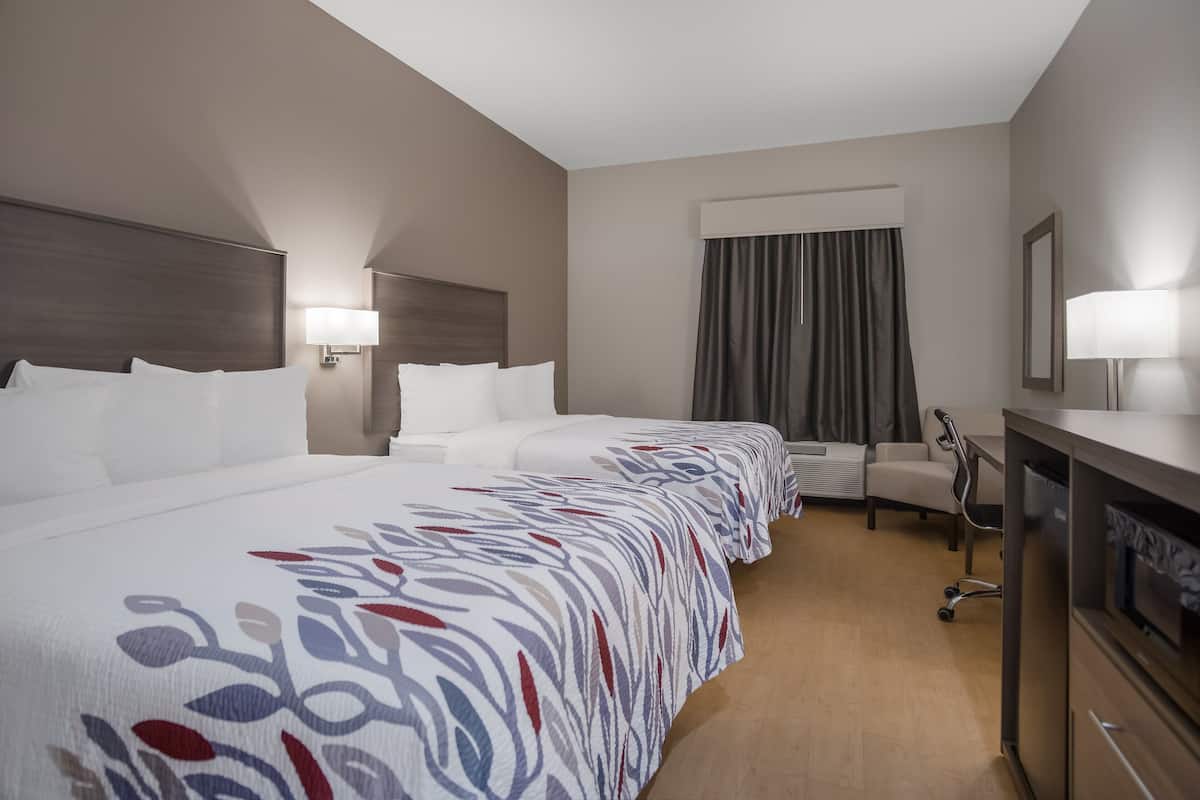 Ett hotellrum med en stor säng, ett skrivbord, en stol, en tv och ett fönster med gardiner.