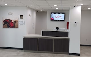 A reception desk with a digital screen displaying a welcome message, a sign prohibiting soliciting, loitering, and trespassing, and a security camera above the desk.