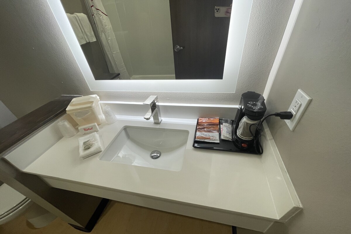 A bathroom with a white sink, a mirror above it, and a coffee maker on the counter.