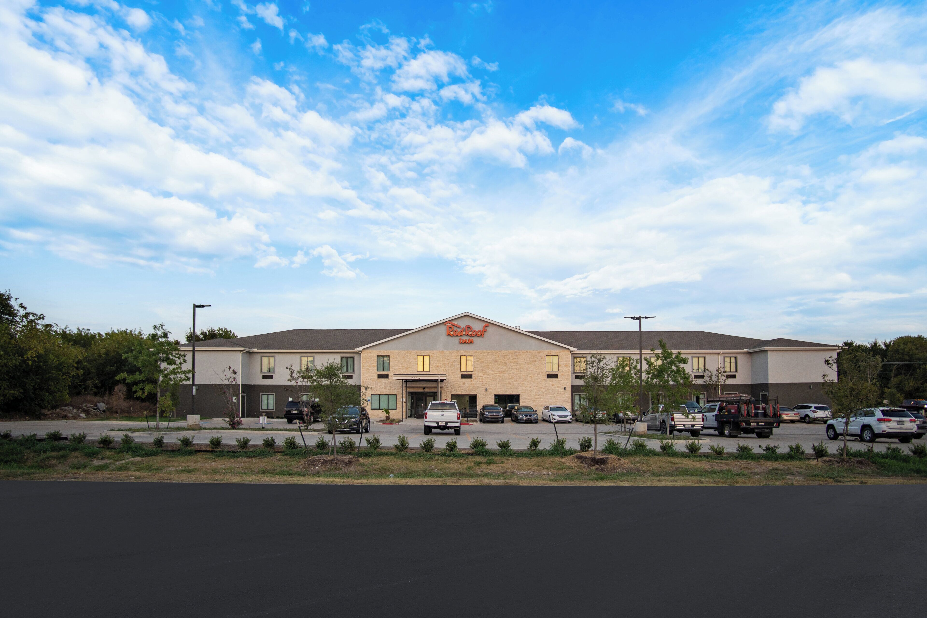 A two-story building with a flat roof, a sign reading 'Roof', and a parking lot with several vehicles.