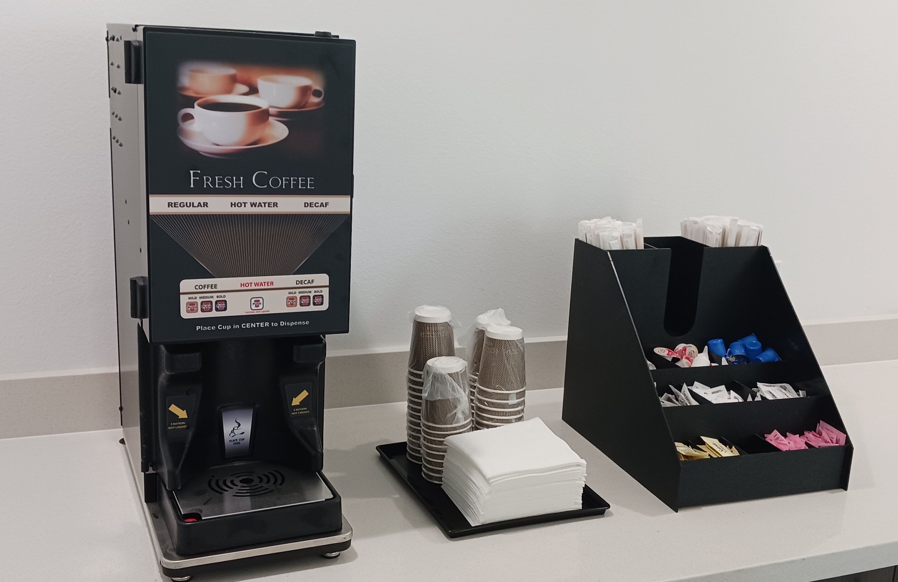A coffee machine with options for regular, hot water, and decaf coffee. There are disposable cups and napkins on the counter.