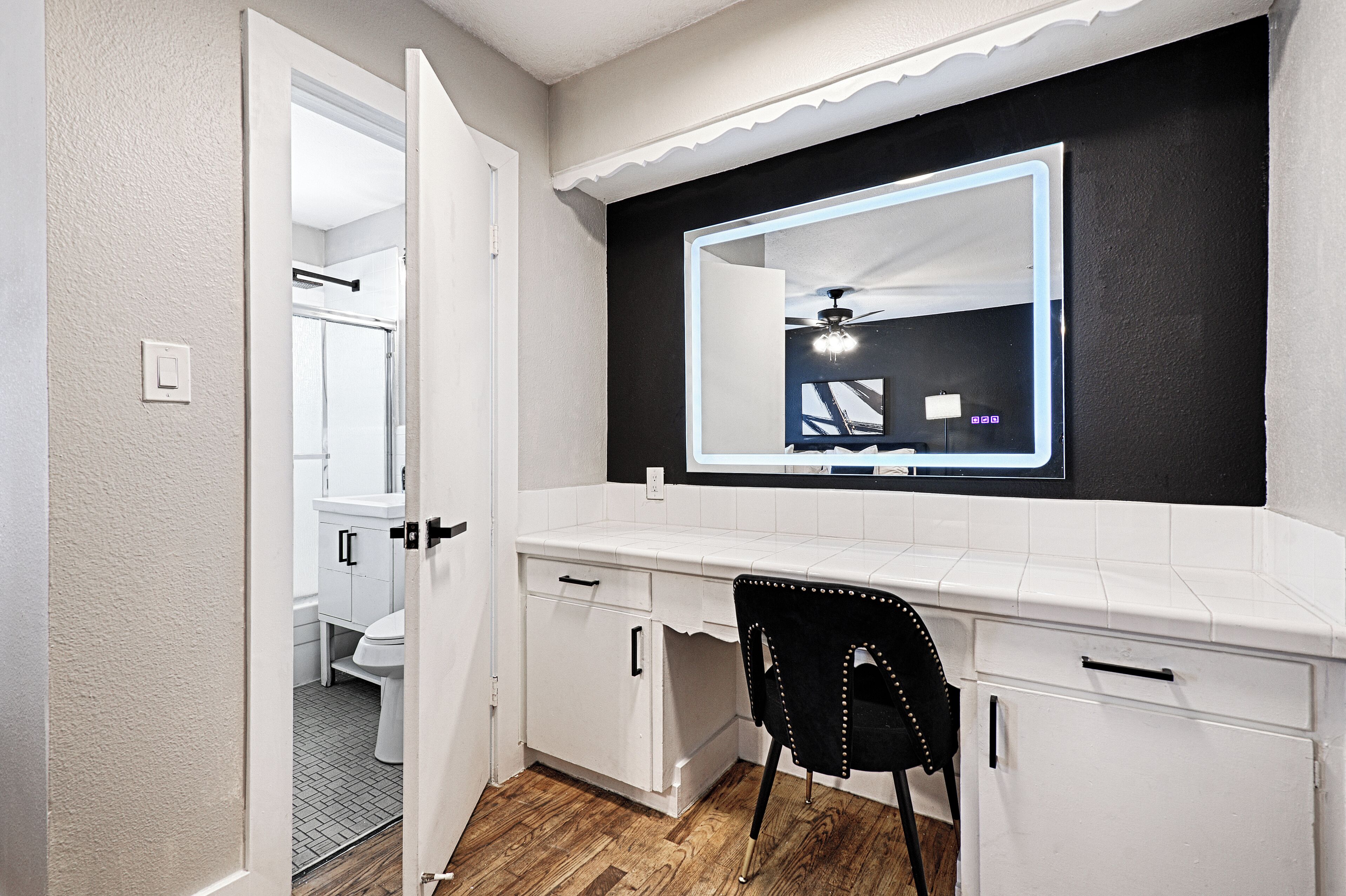 A bathroom with a white vanity, a black chair, and a mirror with a black frame.