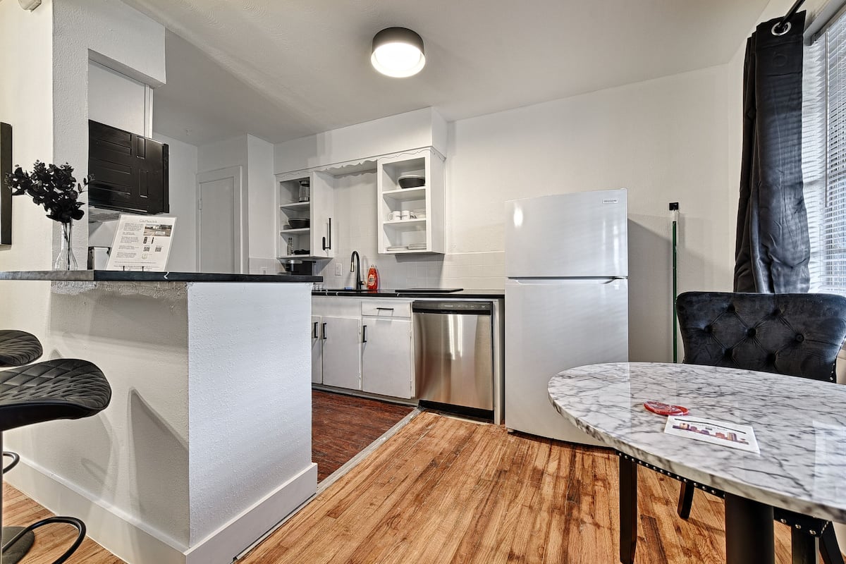 A modern kitchen with white cabinetry, a stainless steel dishwasher, and a marble dining table.