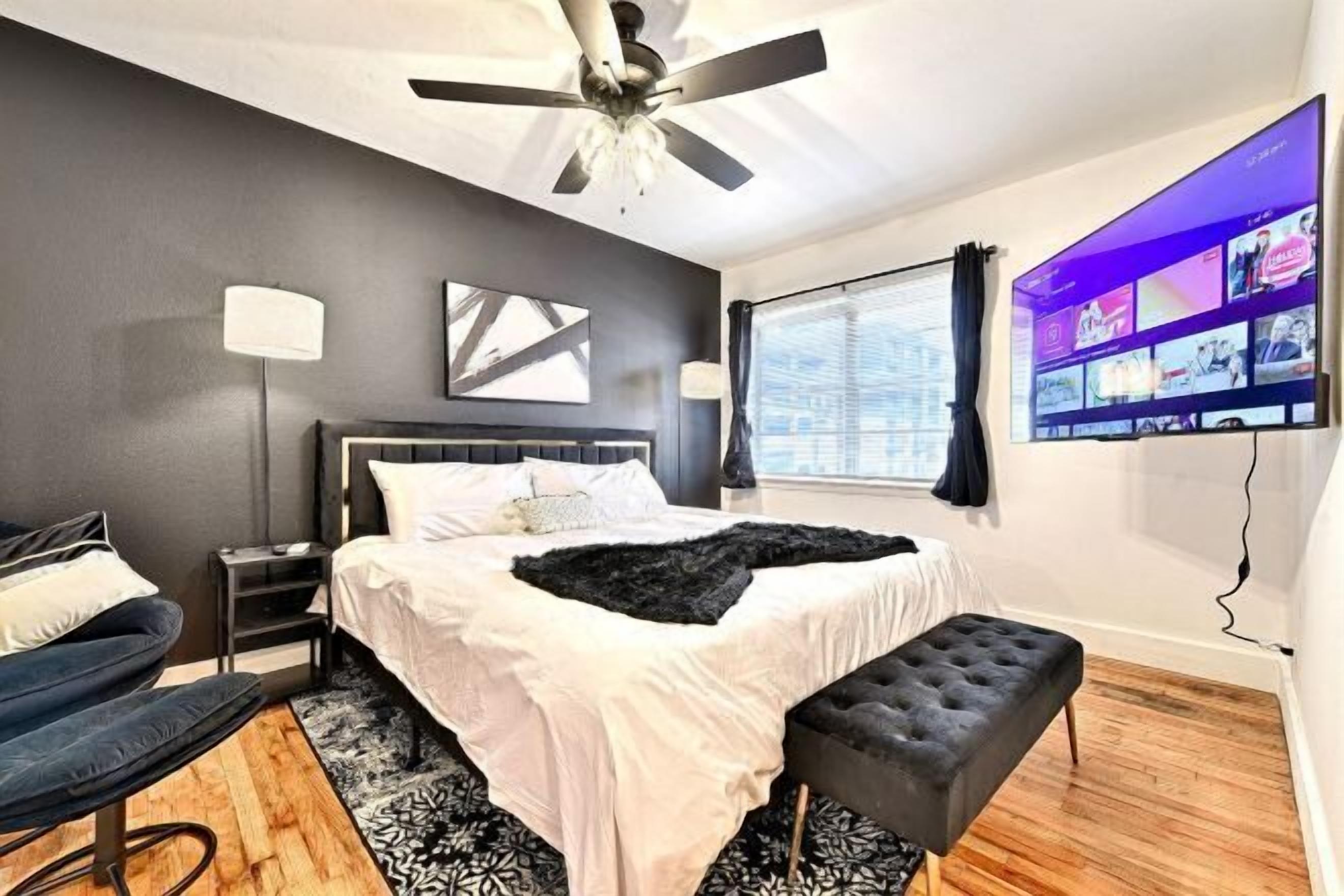 A modern bedroom with a bed, a ceiling fan, a TV, and a window.