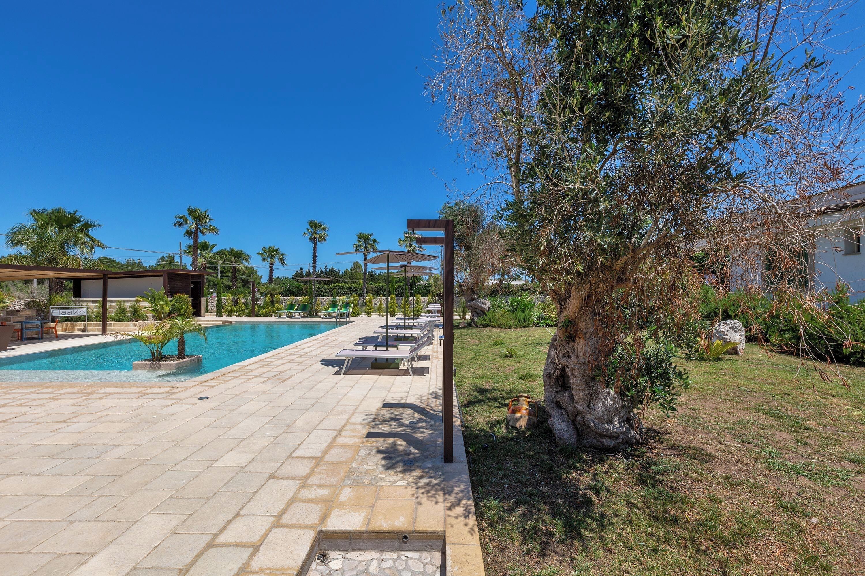 A swimming pool with lounge chairs, a pergola, and a well-maintained lawn.