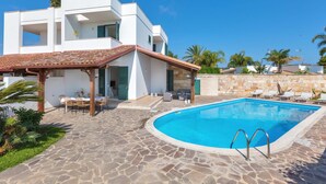 A modern two-story house with a swimming pool, stone patio, and outdoor seating area.