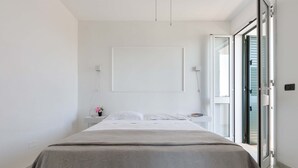 A minimalist bedroom with a bed, a bedside table, and a view through an open door.