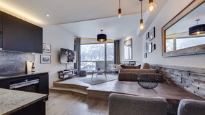 Uma sala de estar moderna com sofá, mesa de centro e área de jantar. Há uma janela grande com vista para árvores e um edifício.