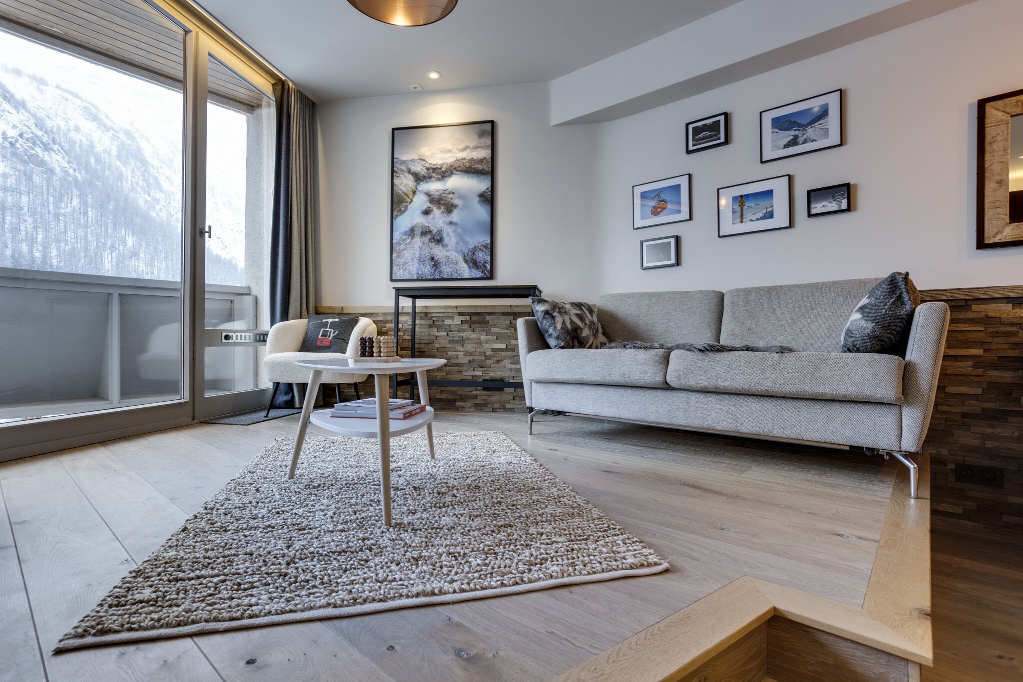 A modern living room with a grey sofa, a white coffee table, and a large window with a view of a snowy mountain.
