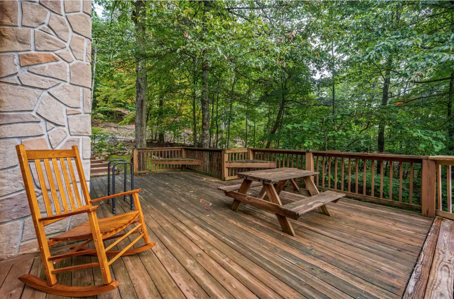 A wooden deck with a stone wall, picnic table, and wooden rocking chair.
