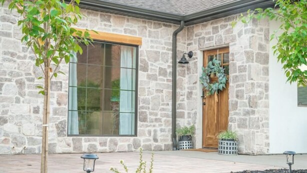A stone building with a large window, a wooden door, and a wreath decoration. - Rustic Gold Retreat (Kanab)