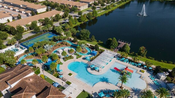 An aerial view of a resort with multiple swimming pools, a lake, and a fountain.