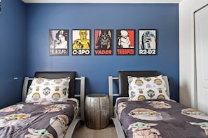 A bedroom with two beds, each with a Star Wars-themed duvet, a wall with Star Wars posters, and a small wooden stool.