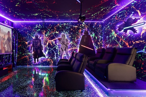 A room with a movie screen, reclining chairs, and a vibrant, colorful wall with abstract designs.