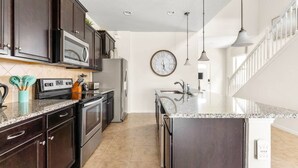 A modern kitchen with dark cabinetry, stainless steel appliances, a granite countertop, and pendant lighting.