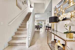 Staircase leads to a dining area with a glass table and chairs, framed artwork, and decorative mirrors.