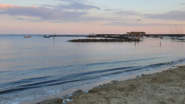 A coastal scene with a sandy beach, calm sea, and a pier with boats.